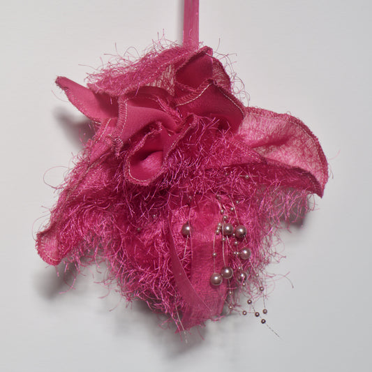 fluffy hot-pink pomander with grey baubles, hanging against a white wall