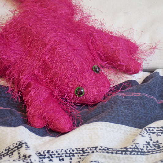 fluffy pink stuffed frog lying on a bed